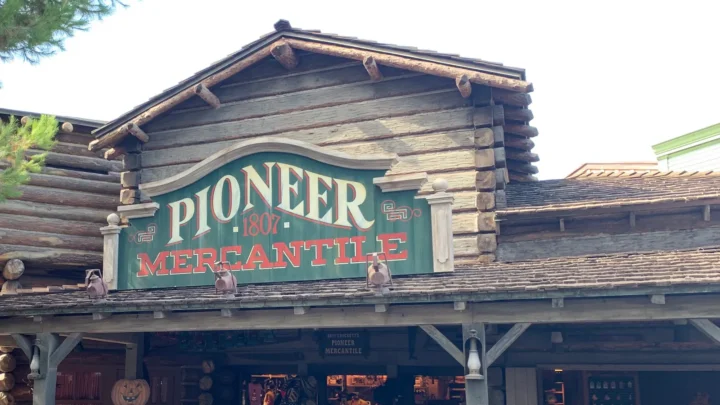 Fachada de madeira da loja Pioneer Mercantile, com placa verde e letras vermelhas, na Frontierland da Disneyland, em Anaheim, na Califórnia, em dia seco (foto de 2019)