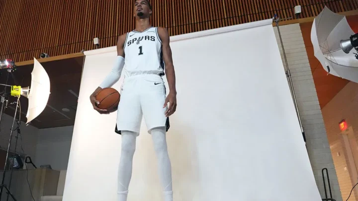 Jogador de basquete com uniforme branco do Spurs segura a bola durante sessão de fotografia em estúdio com iluminação profissional