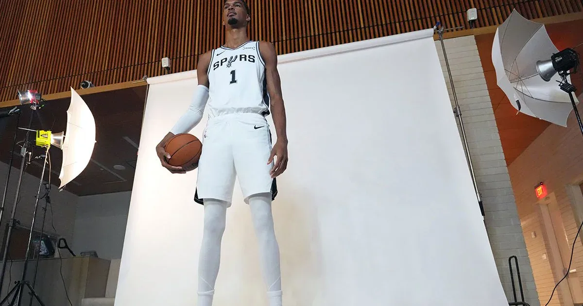 Jogador de basquete com uniforme branco do Spurs segura a bola durante sessão de fotografia em estúdio com iluminação profissional