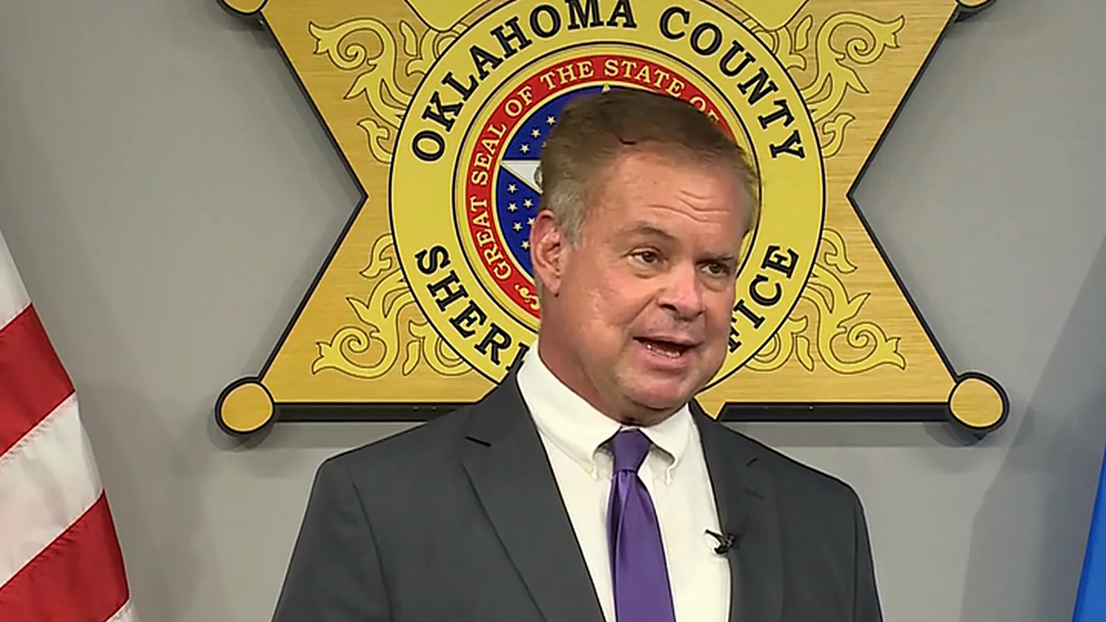 Aaron Brilbeck, porta-voz do Gabinete do Xerife do Condado de Oklahoma, fala à imprensa diante do brasão do xerife