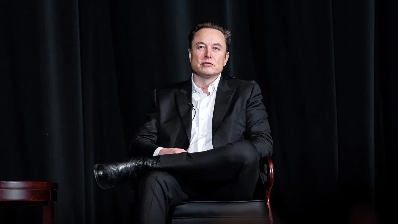 Elon Musk, de terno escuro, sentado em uma poltrona diante de cortinas pretas, em evento na Academia da Força Aérea dos EUA, em abril de 2022