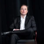 Elon Musk, de terno escuro, sentado em uma poltrona diante de cortinas pretas, em evento na Academia da Força Aérea dos EUA, em abril de 2022