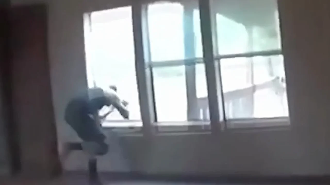 Imagem da câmera corporal mostra o suspeito, de costas, atravessando a janela fechada da sala de uma casa desocupada em Oklahoma
