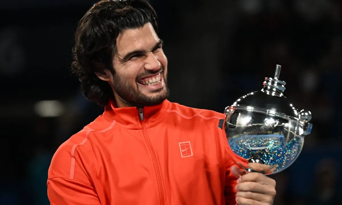 Tenista segura troféu de cristal enquanto sorri em comemoração de vitória em torneio ATP 500