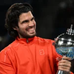 Tenista segura troféu de cristal enquanto sorri em comemoração de vitória em torneio ATP 500