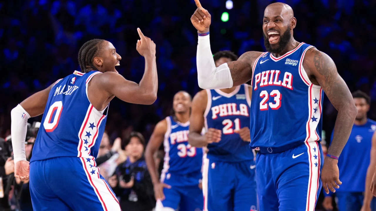 Jogadores do Philadelphia 76ers comemoram com gestos animados durante partida da NBA, com torcedores ao fundo