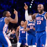 Jogadores do Philadelphia 76ers comemoram com gestos animados durante partida da NBA, com torcedores ao fundo