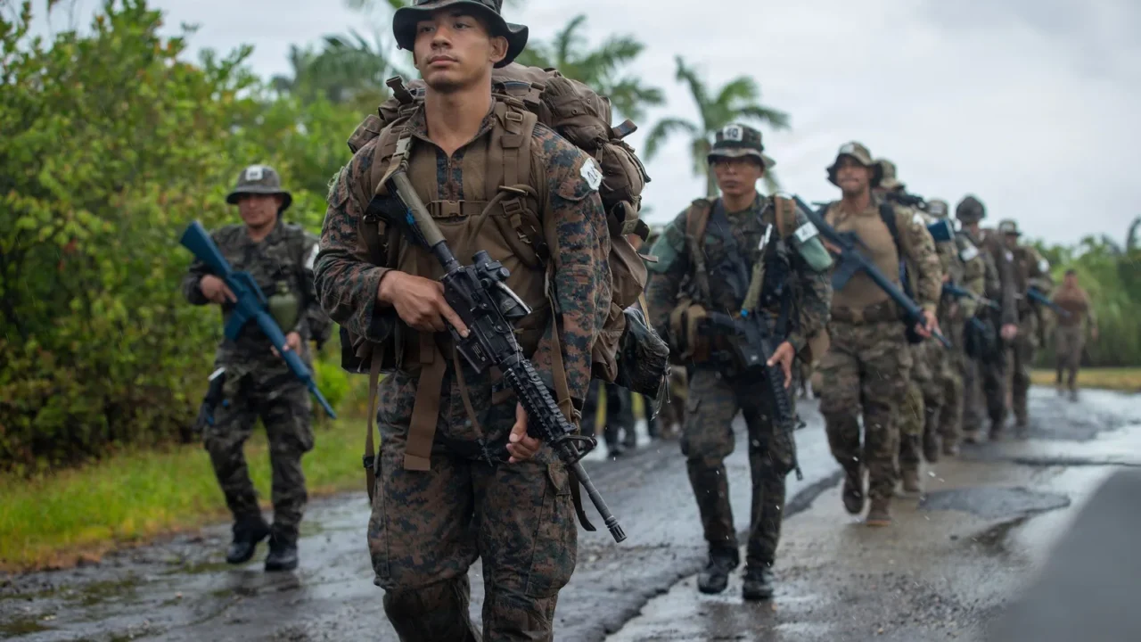 Militares americanos e panamenhos armados caminham em fila por uma estrada molhada, a caminho de uma área de treinamento do curso de operações na selva na Base Aeronaval Cristóbal Colón, no Panamá, em fevereiro de 2026
