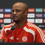 Treinador do Bayern de Munique, de camisa vermelha com o escudo do clube, fala em entrevista coletiva diante de painéis de patrocinadores