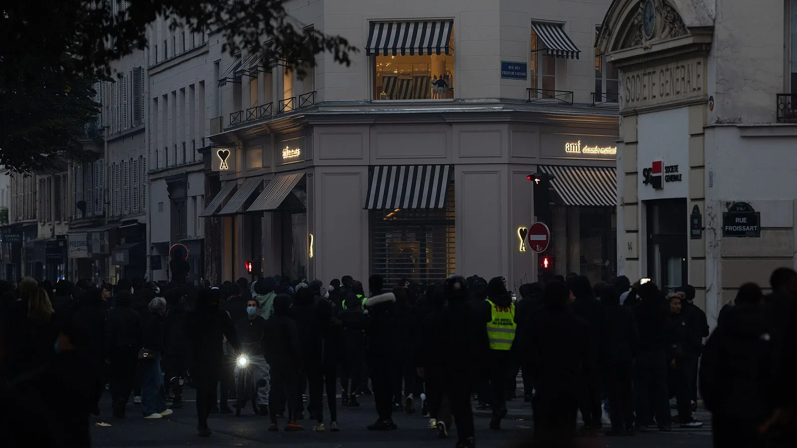 Multidão de encapuzados ocupa um cruzamento diante de prédios e lojas de Paris, em 17 de outubro de 2026