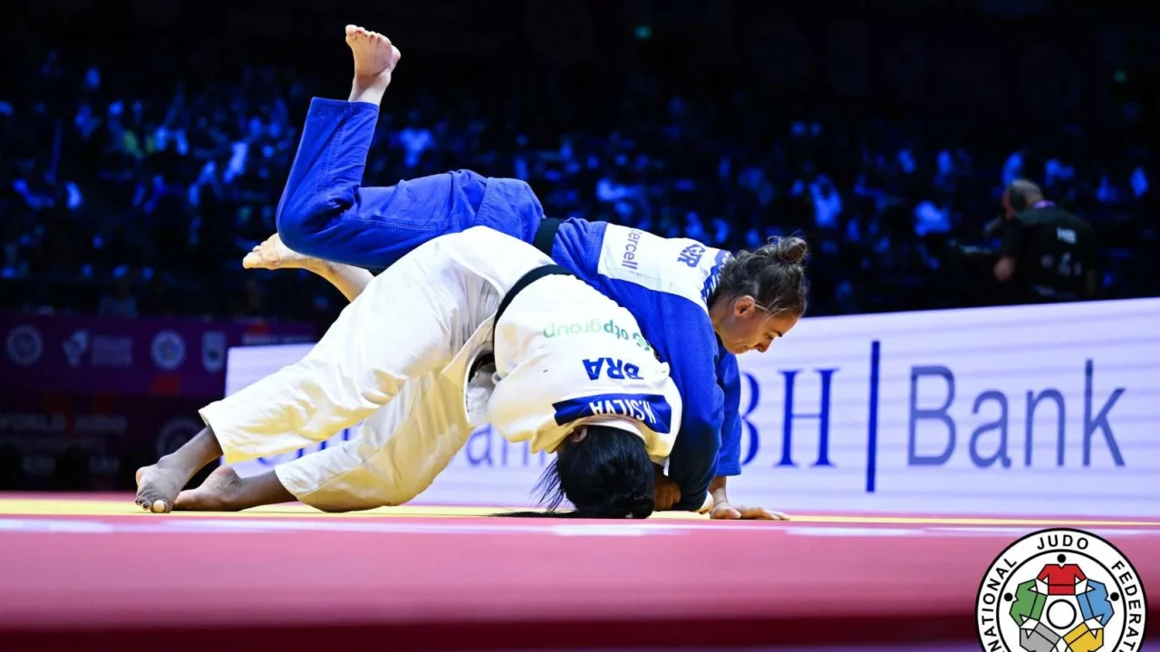 Judoca de faixa azul projeta a adversária de branco sobre o tatame durante combate do Mundial de judô, com plateia ao fundo