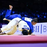 Judoca de faixa azul projeta a adversária de branco sobre o tatame durante combate do Mundial de judô, com plateia ao fundo