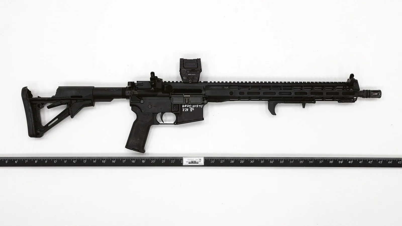 Fuzil semiautomático preto recuperado pelo FBI no local dos tiros em Butler, fotografado sobre fundo branco ao lado de uma régua