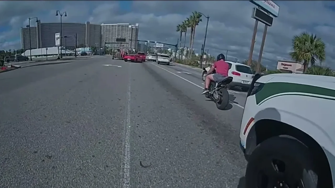 Câmera corporal do policial mostra o motociclista de camiseta vermelha e capacete ao lado de uma viatura do xerife, em uma avenida do Condado de Bay
