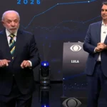 Flávio Bolsonaro e Lula em pé no palco do debate da Band, diante do painel com linhas azuis