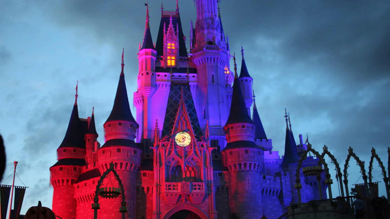 Foto de arquivo do castelo do Magic Kingdom iluminado em vermelho e azul, com céu nublado ao anoitecer, durante a festa de Halloween