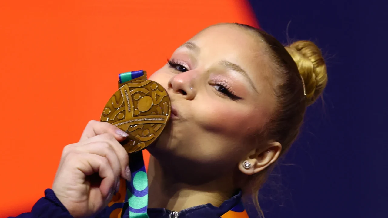 Atleta de ginástica beija medalha de bronze, com uniforme azul e fundo laranja e azul ao fundo