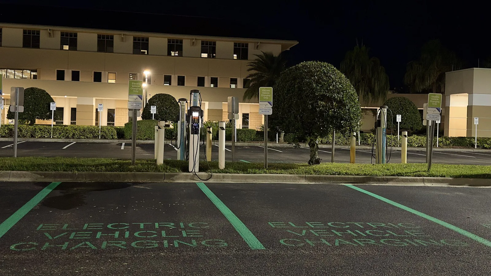 Vagas de recarga para carros elétricos, com carregadores e a inscrição "Electric Vehicle Charging" pintada no chão, à noite, na Flórida