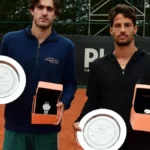 Dois tenistas posam com troféus e relógios durante cerimônia de premiação de torneio de tênis em quadra de saibro