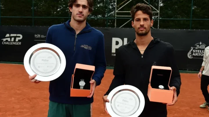 Dois tenistas posam com troféus e relógios durante cerimônia de premiação de torneio de tênis em quadra de saibro