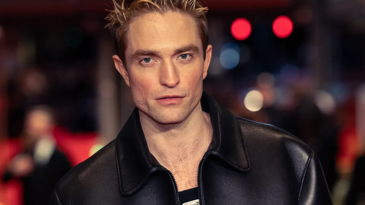 Robert Pattinson, protagonista de 'The Batman Parte II', usa jaqueta preta em evento com luzes desfocadas ao fundo