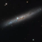 Esta imagem do Telescópio Espacial Hubble da NASA mostra a galáxia espiral intermediária NGC 1827, vista de perfil. Suas faixas de poeira castanho-avermelhadas atravessam a galáxia em todo o seu comprimento. Procure galáxias distantes que pontilham o fundo negro, enquanto um punhado de estrelas em