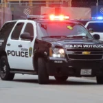 Viatura do Departamento de Polícia de Houston com as luzes de emergência acesas numa rua do centro da cidade, com um policial de costas ao lado (imagem de arquivo, de abril de 2021)