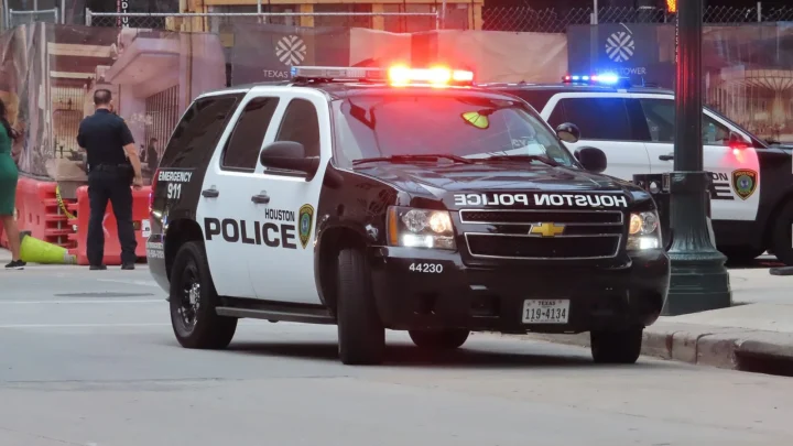 Viatura do Departamento de Polícia de Houston com as luzes de emergência acesas numa rua do centro da cidade, com um policial de costas ao lado (imagem de arquivo, de abril de 2021)