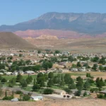 Foto de arquivo (2009): vista de Hurricane, no Utah, com casas, árvores e um cemitério gramado no vale e montanhas e rochas avermelhadas ao fundo, em dia seco