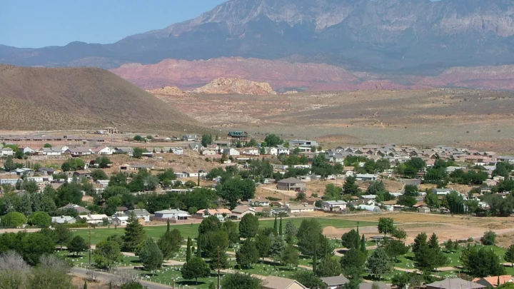 Foto de arquivo (2009): vista de Hurricane, no Utah, com casas, árvores e um cemitério gramado no vale e montanhas e rochas avermelhadas ao fundo, em dia seco