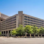 Edifício J. Edgar Hoover, sede do FBI, em Washington, com árvores na calçada e céu azul, em 2024 (imagem de arquivo)
