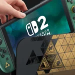 Mão segurando console Nintendo Switch 2 com controles laterais em tom verde e dock com design geométrico dourado e preto com símbolos de Zelda