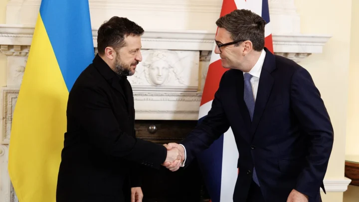 Volodymyr Zelensky, de preto, cumprimenta o primeiro-ministro britânico, Andy Burnham, diante de uma bandeira da Ucrânia e de uma do Reino Unido, em Londres, em outubro de 2026