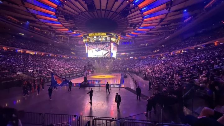 Madison Square Garden lotado, com luzes azuis e laranja no teto e a quadra iluminada, durante evento dos Knicks nas finais de 2026