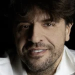 Retrato do neurocientista Karl Deisseroth, de camisa branca, sorrindo sobre fundo escuro