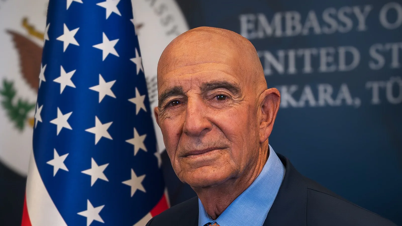 Retrato oficial de Tom Barrack, embaixador dos EUA na Turquia, diante da bandeira americana e do painel da embaixada em Ancara