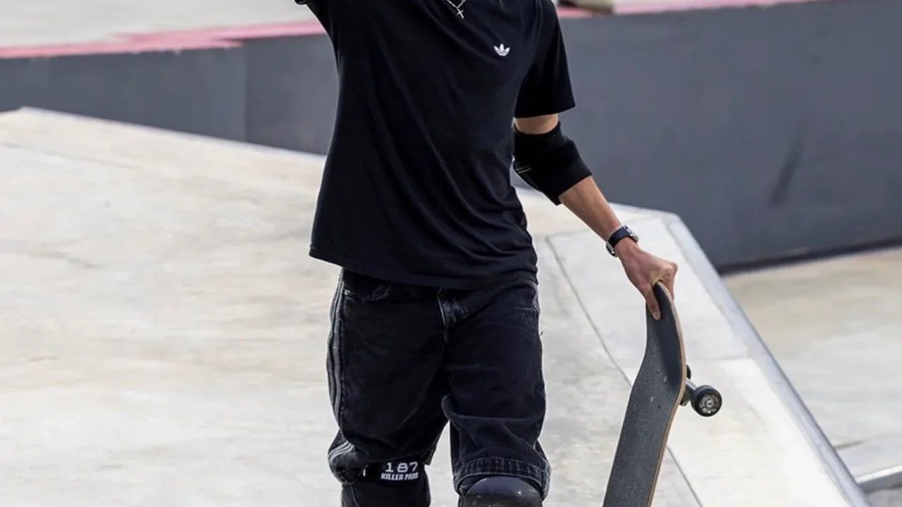 Skatista comemora com o punho erguido em pista de skate park, usando capacete Red Bull e joelheiras, com prancha na mão