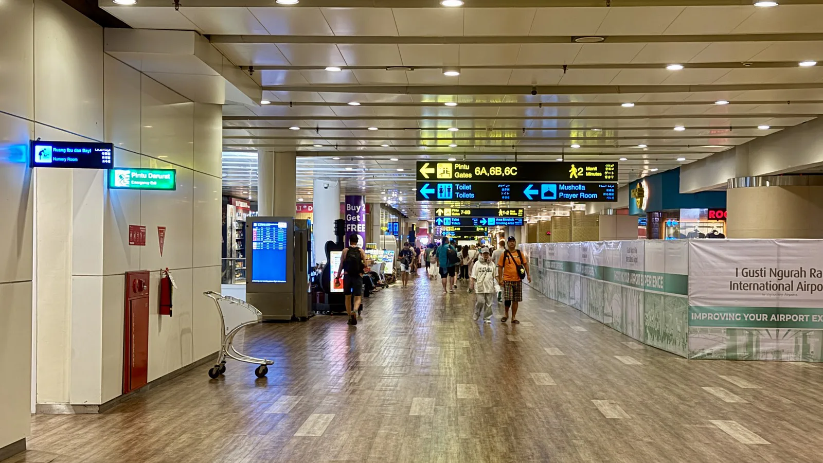 Corredor do terminal internacional do aeroporto de Bali, com placas de embarque e passageiros caminhando com malas