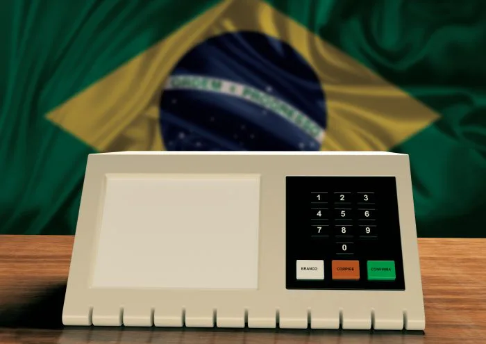 Urna eletrônica diante da bandeira do Brasil. Cerca de 265 mil eleitores brasileiros registrados nos Estados Unidos votam neste domingo, 4 de outubro, no primeiro turno das Eleições 2026.