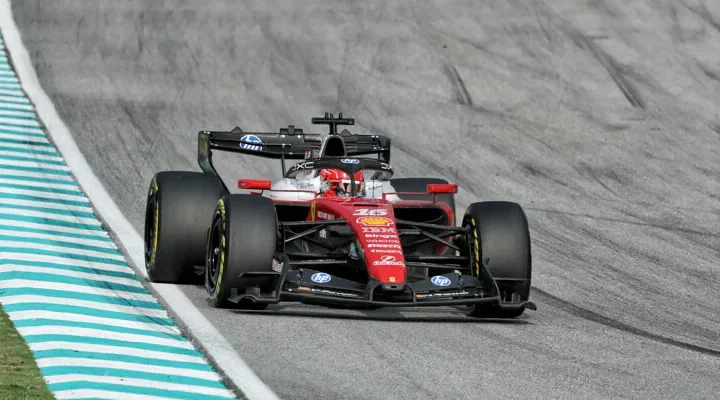 Carro vermelho de Fórmula 1, com pintura da Ferrari, acelera em pista de asfalto ao lado de zebras azuis e brancas na curva