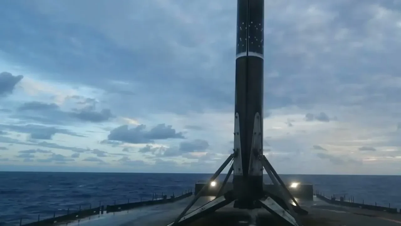 Primeiro estágio do Falcon 9 em pé, com as pernas de pouso abertas, no convés da balsa no meio do oceano Atlântico, sob céu nublado