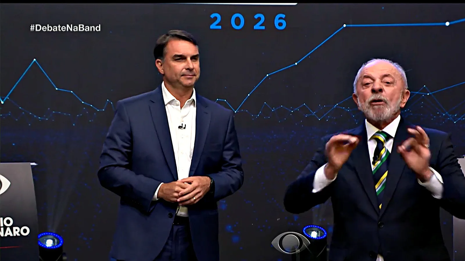 Flávio Bolsonaro e Lula lado a lado no palco durante o primeiro confronto direto