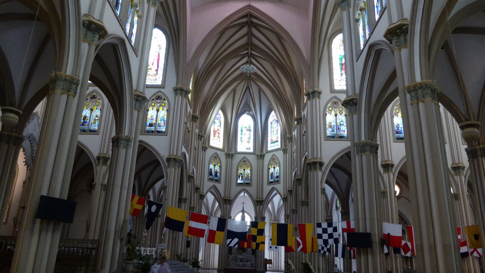 Arcos neogóticos e vitrais do interior da Catedral de Guayaquil, com fileiras de bancos e bandeirolas penduradas entre as colunas (foto de arquivo)