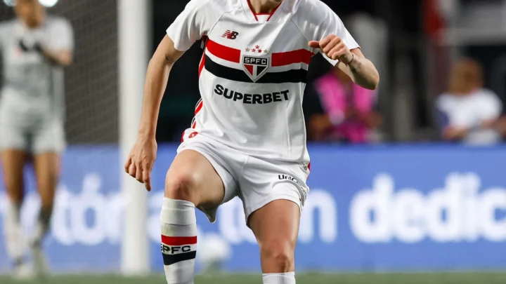 Jogadora de futebol feminino controla a bola durante partida do Brasileirão, usando uniforme branco com faixa vermelha e preta e patrocinador Superbet