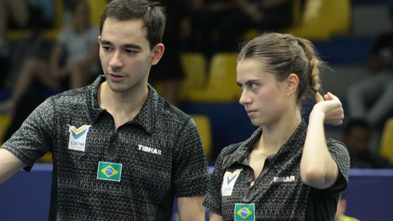 Dupla brasileira de tênis de mesa durante competição, com uniformes pretos e emblema do Brasil na altura do peito