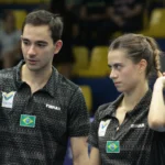 Dupla brasileira de tênis de mesa durante competição, com uniformes pretos e emblema do Brasil na altura do peito