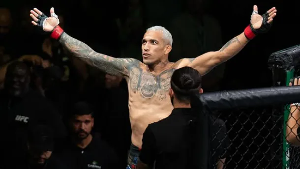 Lutador tatuado comemora vitória dentro do octógono com os braços levantados e luvas vermelhas durante evento de artes marciais mistas