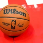 Bola oficial da NBA com tecnologia integrada para coleta de dados em tempo real, posicionada sobre quadra vermelha