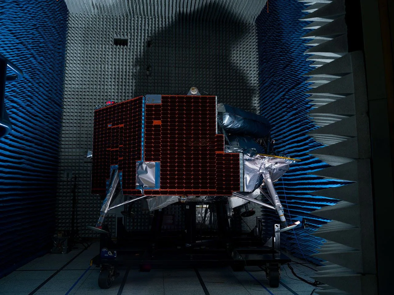 A Figura B mostra a Griffin-1 em 29 de julho em uma câmara anecoica para testes de interferência eletromagnética e compatibilidade eletromagnética, que garantem que os sinais dos componentes eletrônicos da espaçonave não interfiram uns nos outros. Longas pontas de espuma revestem as paredes da câmara para absorver ondas sonoras e ondas eletromagnéticas.