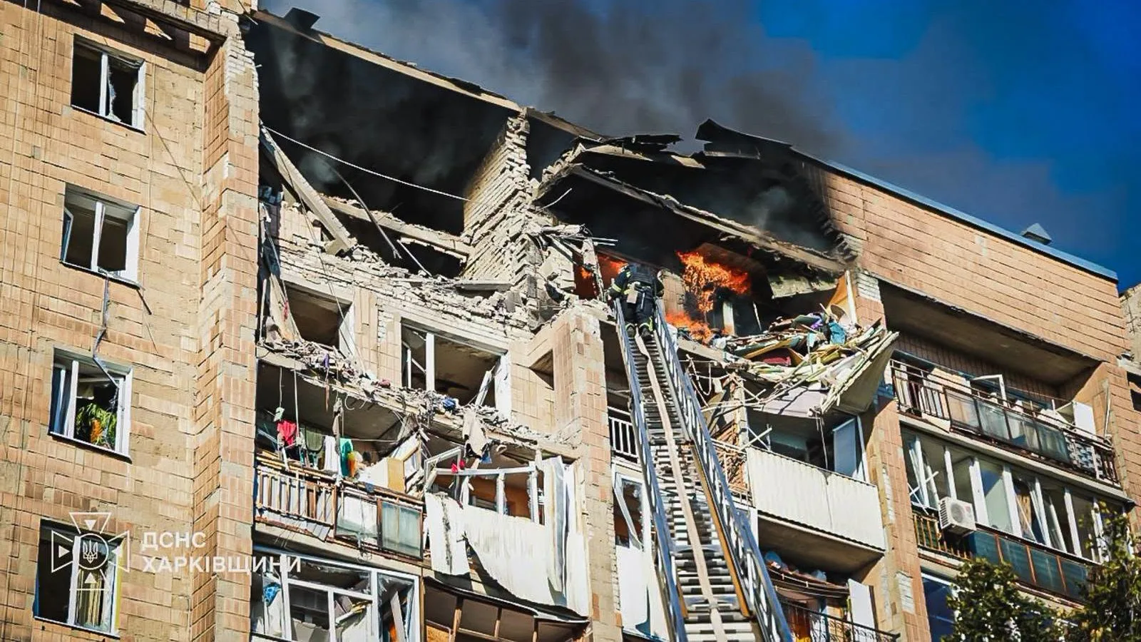 Bombeiro em escada diante de prédio residencial destruído e em chamas no distrito de Kyivskyi, em Kharkiv, atingido por drone em 12 de outubro de 2026